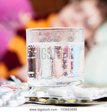 Glass With Dissolved Drug In And Pills On Table