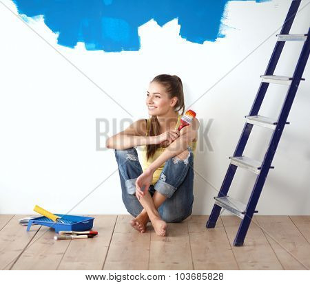 Portrait of female painter sitting on floor near wall after painting.