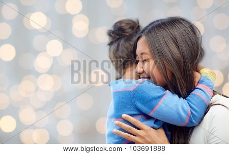 family, children, love and happy people concept - happy mother and daughter hugging over lights background