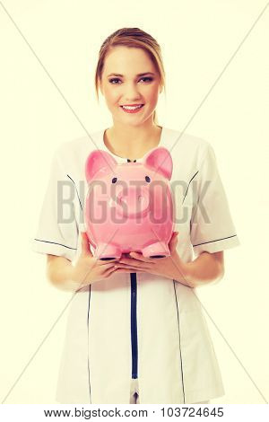 Young beautiful female doctor holding a piggybank.