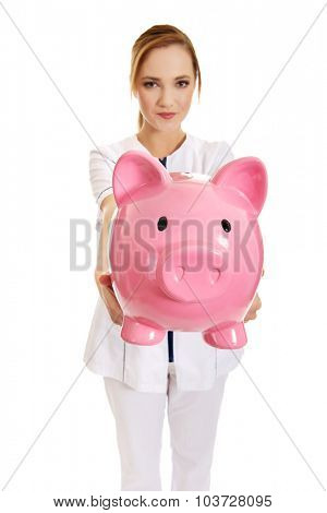 Young beautiful female doctor holding a piggybank.