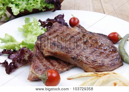 meat food : roast steak boneless with roast onion and red hot peppers, served on green lettuce salad on dish isolated over wooden table