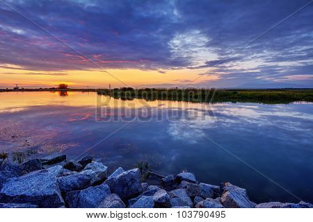 Serene waters, rocks on the foreground, and the sunset on the horizon