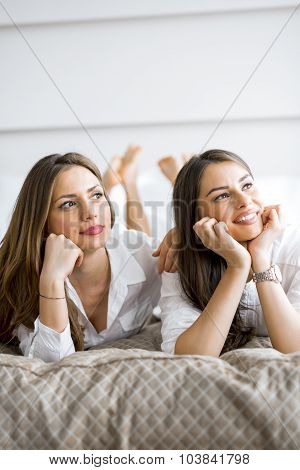 Two Beautiful Girls Talking And Smiling While Lying On A Bed