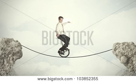 Brave business man riding an mono cycle between cliffs concept