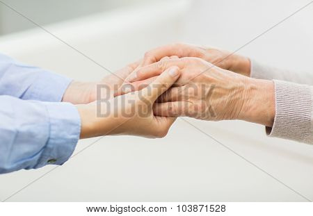 people, age, family, care and support concept - close up of senior and young woman  holding hands