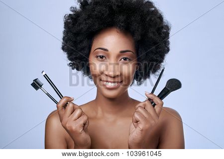 Beautiful black african afro model with flawless complexion and smooth skin holding up different make-up brushes for different applications