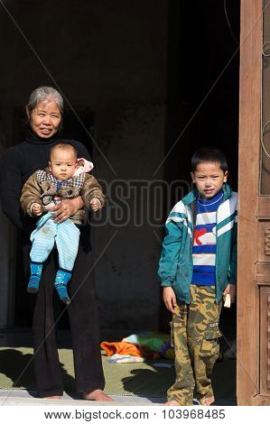 MAI CHAU, VIETNAM, DECEMBER 12, 2014: A happy Chinese grandmother and her grandchildren are enjoying the sunlight at the home entrance in the village of Mai Chau, Vietnam