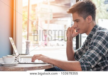 Businessman Using Mobile Phone While Lookingat Laptop On Wooden Table In Coffee Shop