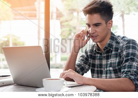 Businessman Using Mobile Phone While Lookingat Laptop On Wooden Table In Coffee Shop