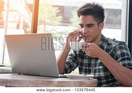 Businessman Using Mobile Phone While Lookingat Laptop On Wooden Table In Coffee Shop