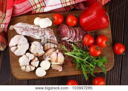 Salami With Cherry Tomatoes, Pepper, Garlic And Ruccola On A Cutting Board