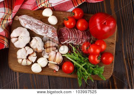 Salami With Cherry Tomatoes, Pepper, Garlic And Ruccola On A Cutting Board
