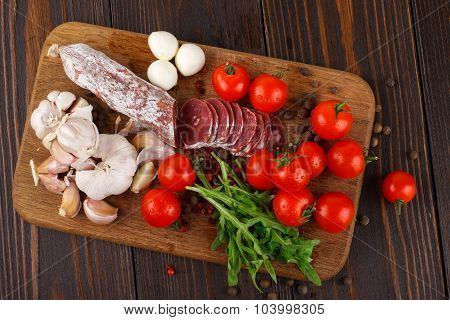 Salami With Cherry Tomatoes, Ruccola And Garlic On A Cutting Board