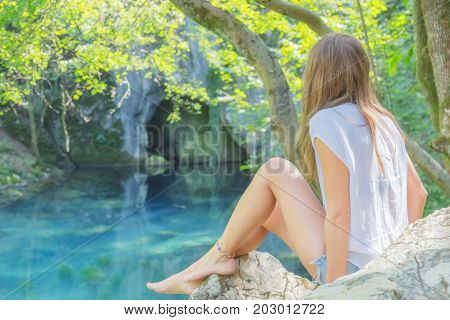 Young woman sitting near the beautiful lake in nature.