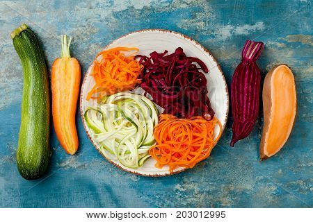 Zucchini carrot sweet potato and beetroot noodles on a plate. Top view overhead. Blue rustic background