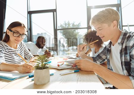 Campus life. Cheerful young students sitting in the cafeteria and doing their home assignment while enjoying students life