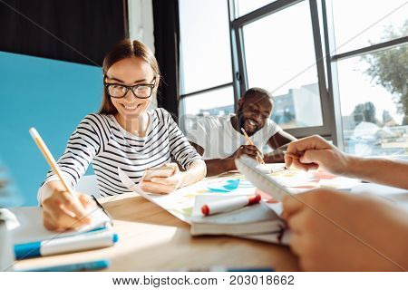 Smart and intelligent. Cheerful beautiful female student sitting at the table in the cafeteria and studying while with her groupmates