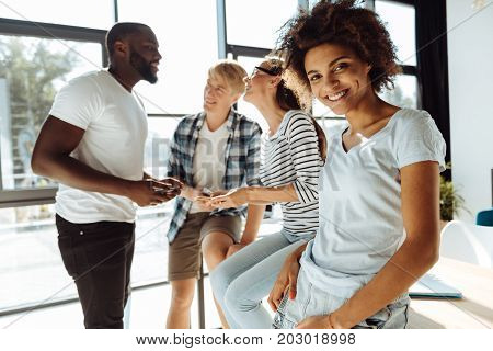 Full of positivity. Cheerful smiling afro american woman leaning on the table while resting with her university friends