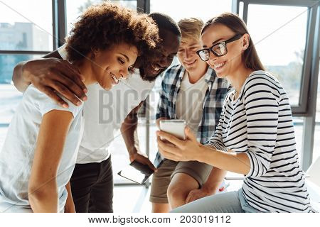 Modern gadgets. Cheerful smiling students using smart phone and resting together while feeling happy