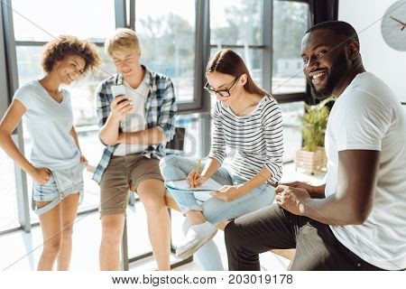 Time for individual activities. Cheerful international students having rest and enjoying their leisure time while using modern gadgets