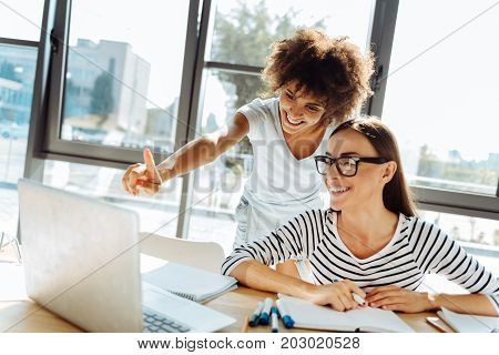 This one. Positive beautiful female friends using the laptop and sitting at the table while studying together
