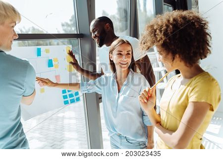 Full of ideas. Cheerful international young colleagues standing in the office and working on their project while feeling happy