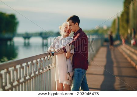 A beautiful blonde in a pink dress with her handsome guy in a red shirt is good at spending time near river