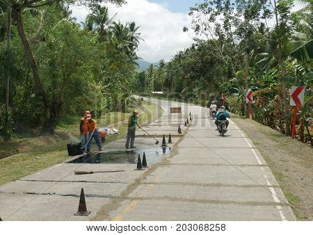 DAVAO ORIENTAL, PHILIPPINES--MARCH 2016: Road workers doing repairs at the national highway to Davao Oriental, southern Philippines on a bright day.