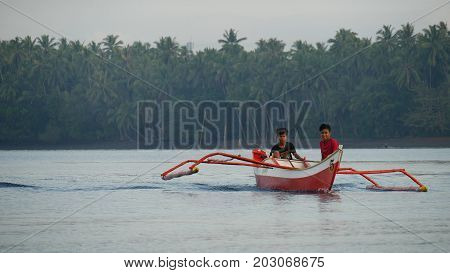 DAVAO ORIENTAL, PHILIPPINES--MARCH 2016: Two boys on a red and white boat fishing in the lagoon of Puntalinao, Davao Oriental, southern Philippines.