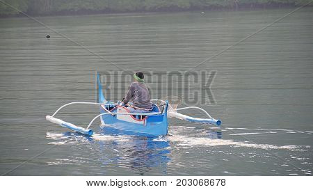 DAVAO ORIENTAL, PHILIPPINES--MARCH 2016: A traditional fisherman heads out to the lagoon in a small fishing boat early in the morning.