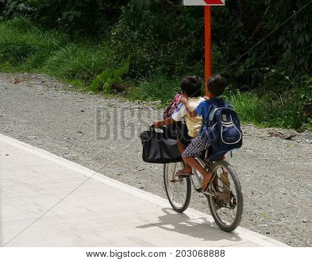 DAVAO ORIENTAL, PHILIPPINES--Two chilcren ride one bicycle from school along the main highway in Davao Oriental in March 2016.