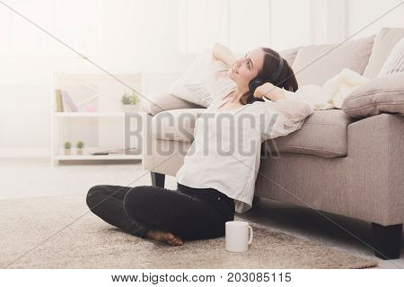 Relaxed girl in headphones on the floor. Young woman in casual listening to music and drinking coffee