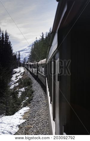 vertical view of train in Alaska with snow on the ground and mountains ahead