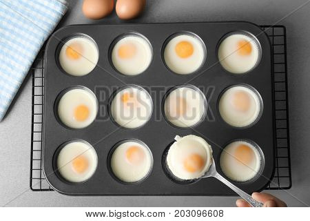 Woman holding spoon with baked egg over muffin tin