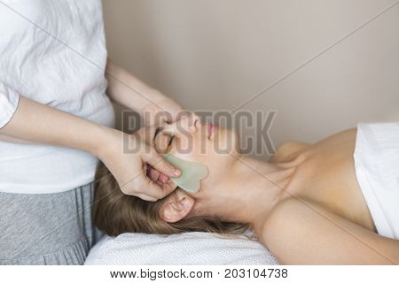 Young woman have face guasha treatment at asian beauty clinic