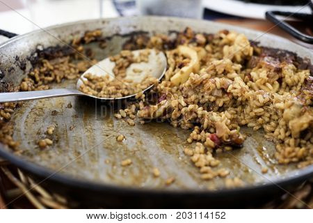 closeup of a paellera, the paella pan, with some spanish seafood paella and a serving spoon, on a table during lunch