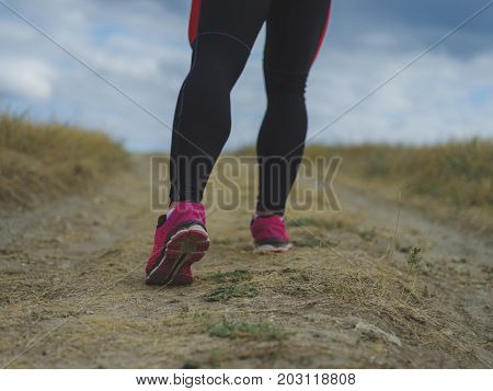 Close-up picture of fit, sporty, muscular legs running on a blurred light natural background. Man walking in black leggings and sneakers. Marathon, jogging, running, training, exercising concept.