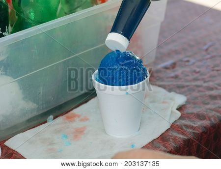 Pouring blueberry syrup onto snow cone at farmer's market