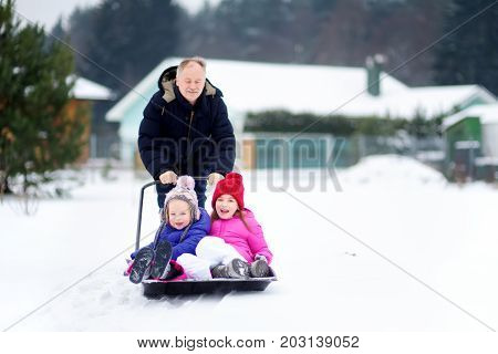 Two funny little sisters having a ride on a snow shovel on chilly winter day. Children playing in a snow during winter break. Winter activities for families.