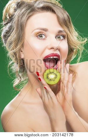Fruit Series. Portrait of Surprised Caucasian Blond Model Posing With Slice of Green Juicy Kiwi Fruit and Opened Mouth. Against Green Background. 