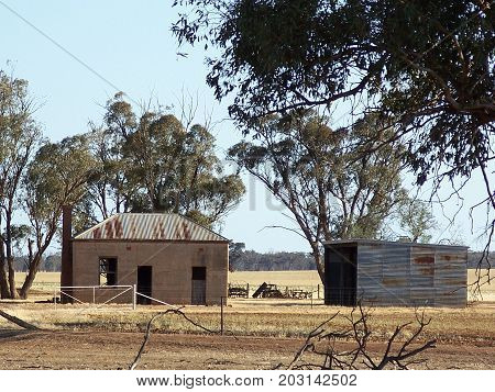 Old clay brick house with corrugated tin roof with wooden shed in dry Australian paddock.