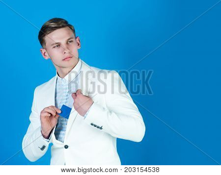Fashion and information concept. Manager wearing casual suit on blue background. Businessman posing in white jacket and shirt. Banking and saving. Man hiding business or bank card copy space