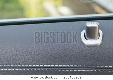 Door handle with lock contol buttons of a luxury passenger car. Black leather interior of the luxury modern car. Modern car interior details
