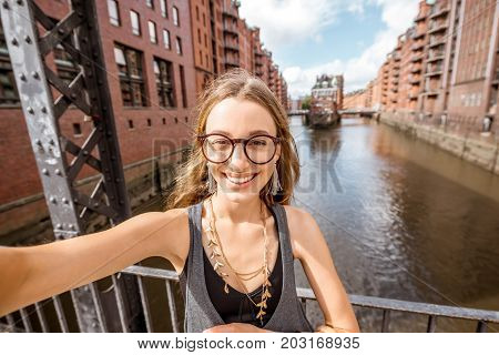 Young woman tourist making selfie photo on the beautiful water channel background in Speicherstadt, historic warehouse district in Hamburg, Germany