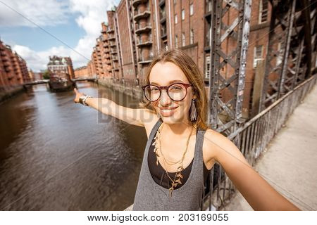 Young woman tourist making selfie photo on the beautiful water channel background in Speicherstadt, historic warehouse district in Hamburg, Germany