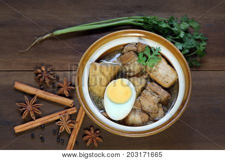 Belly Pork Chinese Five-Spice Stew with boiled egg and tofu decorated with anise star, black pepper, cinnamon and coriander on wooden background, asia food.