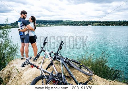 cuple of sportmen sitting near lake with bicycles and showing thumb up