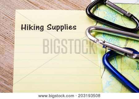 Hiking Supplies list concept on notebook and wooden board with carabiners