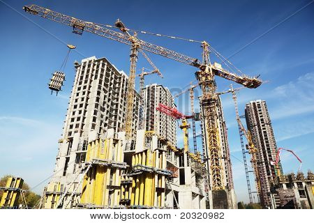 Arbejder på plads med mange høje bygninger under opførelse og kraner under en blå himmel